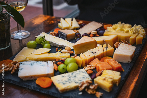 Photos Assorted cheese board with grapes, nuts and dried fruit served on a slate platter in a restaurant setting