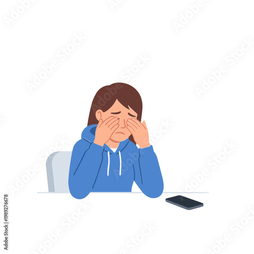 Woman sits at table rubbing eyes with hands covering face next to phone