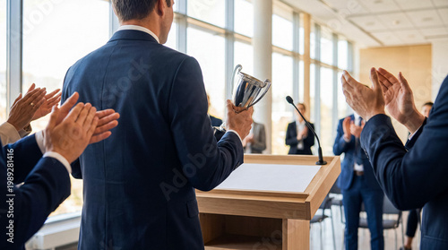Tableau sur toile Successful businessman holding a silver trophy cup, viewed from behind at a corporate event
