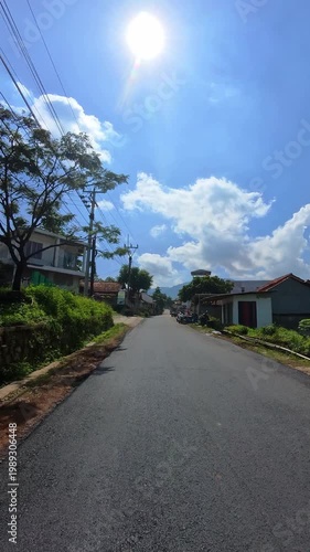 First-person video of a motorcycle ride on a sunny day on a countryside road that rises upwards and is surrounded by trees and plantations. Footage riding on the hinterland of Bandung, Indonesia