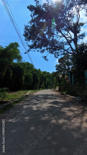 First-person video of a motorcycle ride on a sunny day on a countryside road that rises upwards and is surrounded by trees and plantations. Footage riding on the hinterland of Bandung, Indonesia