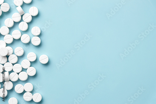 White pills scattered on light blue background, pharmacy and healthcare medication concept with ample copy space in minimalist flat lay.