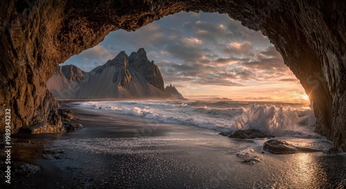 A breathtaking view of a rugged coastline and towering mountains is framed by a natural rock arch, bathed in the warm glow of a setting sun.