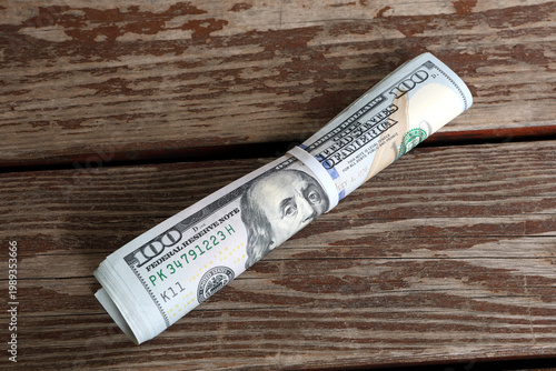 Quadro su tela Roll of One Hundred US Dollar Bills with Rubber Band on Wood