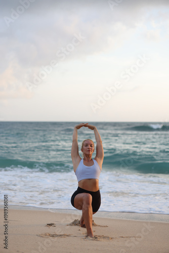 Sunrise atop tranquil shoreline. Peaceful scene of blonde woman in headstand during sunrise at shoreline