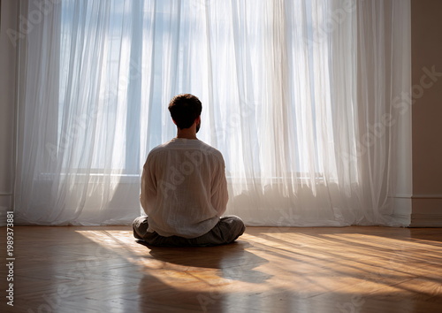 Man of Middle-Eastern descent meditating in sunlit room by a window with white curtains