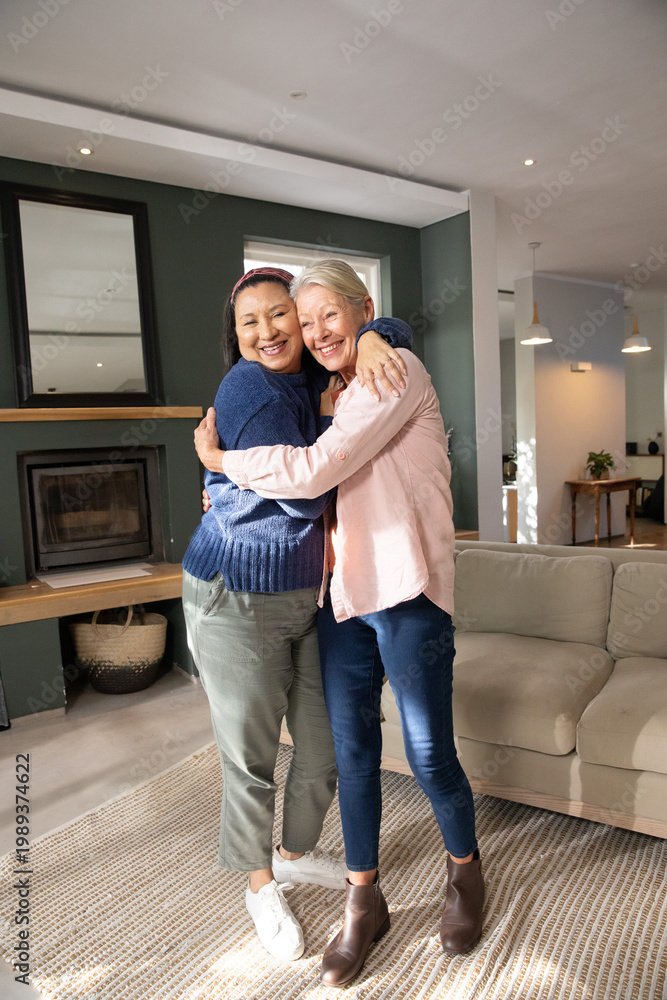 Fototapeta premium Diverse mature female friends hugging, standing on textured woven rug in bright living room