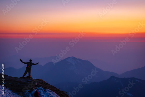 Photography A person stands on a mountain peak at sunset with arms outstretched overlooking
