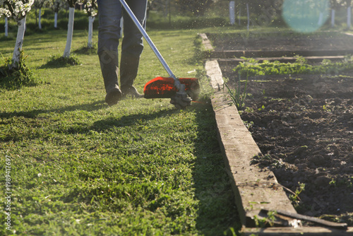 Quadro su tela Man Trimming Grass With String Trimmer in Countryside Yard – Spring Work and Lif