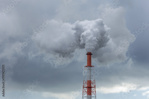 Cuadro en lienzo Tall red and white industrial chimney releases a dense, billowing plume of white-gray smoke into a heavy, grey overcast sky, illustrating air quality, industrial emissions, and environmental impact