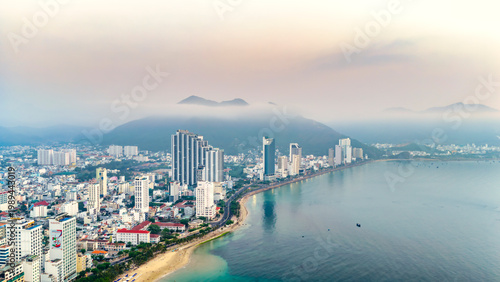 Photography A serene aerial view of Nha Trang city, Vietnam during early morning, where a gentle layer of mist lingers over the mountains and coastline