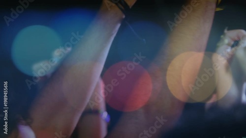 Audience responding to music beat, raising and clapping with yellow band and glasses over bokeh