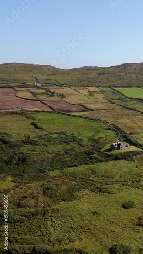 Idyllic Irish countryside with vibrant green fields and distant houses dotting the rugged rolling hills on a clear sunny day.
