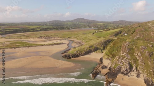 Morning light illuminates a winding river as it carves its way across a broad sandy beach, merging with the crashing waves of the Atlantic Ocean along the stunning coast of Ireland.