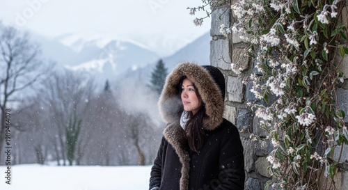 Woman in winter coat standing by stone wall with snowy mountain background