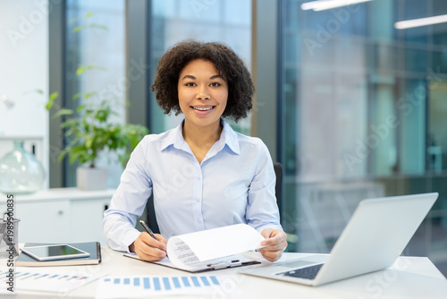 Obraz na plátně Portrait of a young African American businesswoman sitting at a desk in the offi