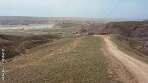 Aerial drone flight over spring steppe with dirt road and Kurty Reservoir, Kazakhstan landscape