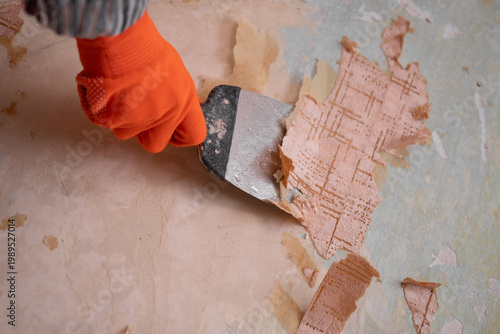 worker's hands are removing wallpaper from wall.