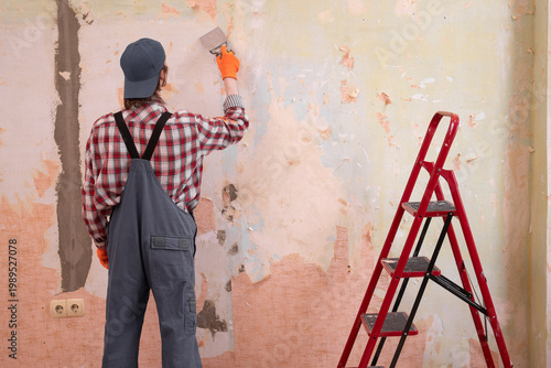 Apartment renovation concept. man tearing off old wallpaper from wall preparing for home redecoration.