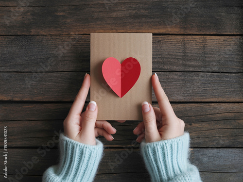 A person holding a brown card with a red heart on a wooden background