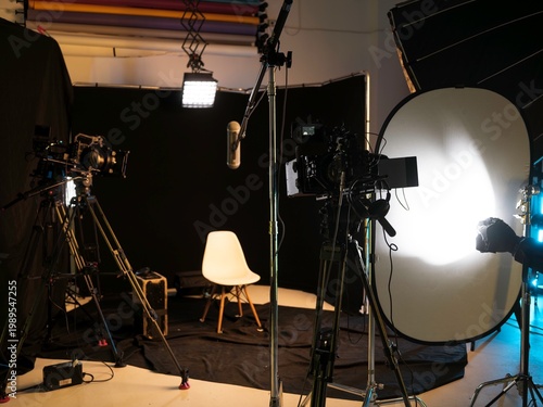 In a sleek podcast studio, cameras are positioned and lights illuminate the scene, creating a vibrant atmosphere for interviews. The space is cozy and well-organized, ready for engaging discussions