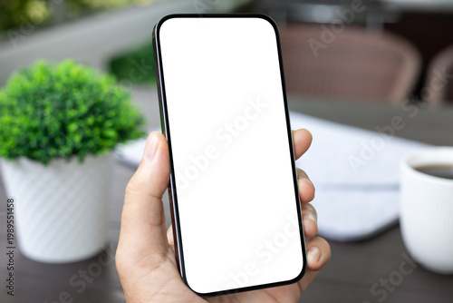 Hand holding smartphone with blank white screen mockup office desk