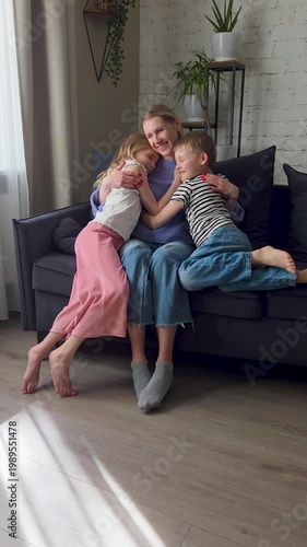 Two kids runs and hug mother on comfortable couch at home living room, happy laughing mom with adorable loving daughter and son. Mothers day, birthday celebration