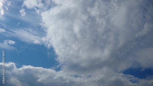 The clouds shift and change shape under the blue sky. Light plays on the clouds as they move, hinting at possible weather changes. This happens during daylight hours above a scenic area.