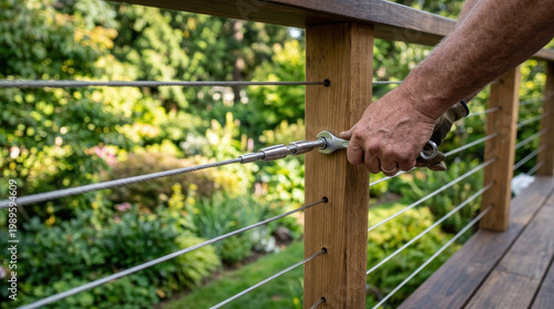Hand installing stainless steel cable railing on wooden deck outdoors, close up of manual tensioning