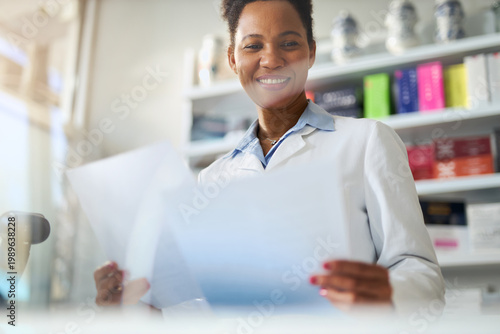 Foto Happy black female  pharmacist reading list of medicine while working in pharmac