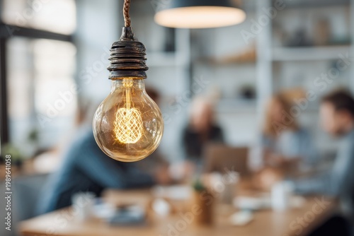 Focused shot of a glowing, old-fashioned lightbulb hanging above a blurred, collaborative meeting