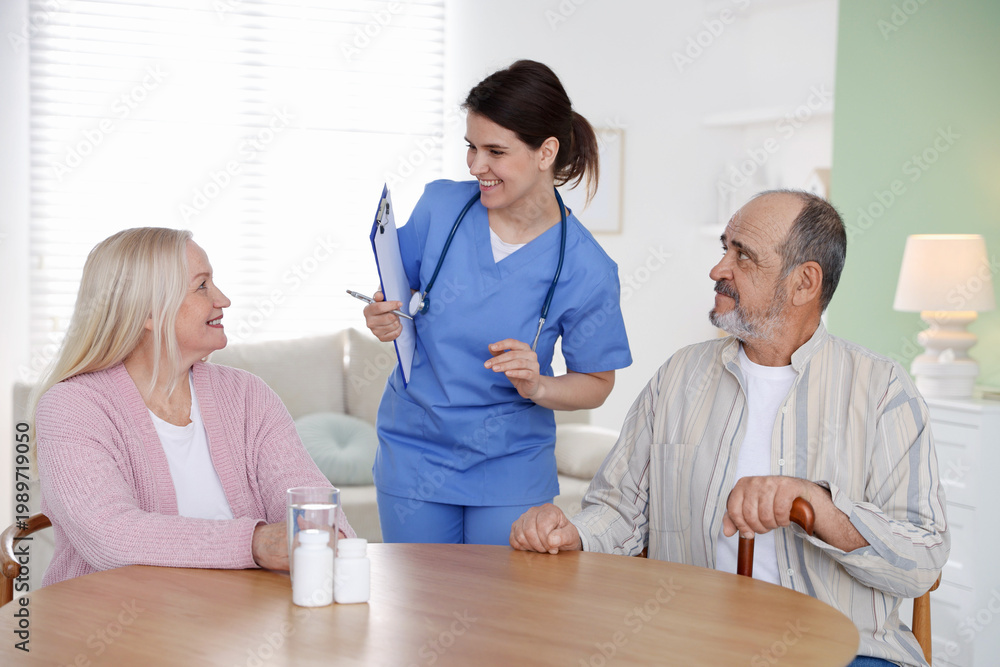 Obraz premium Smiling care worker with clipboard working with senior couple at wooden table at nursing home