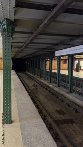 Vertical footage of a classic yellow subway train entering a historic underground station. Features iconic green metal pillars and clean platform architecture.