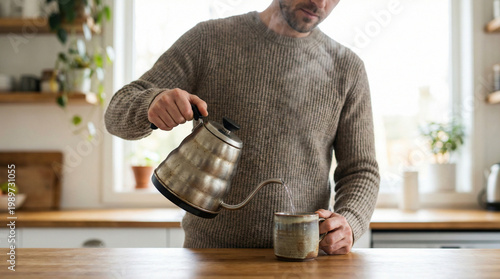 Man pouring hot water into teacup in modern kitchen setting  