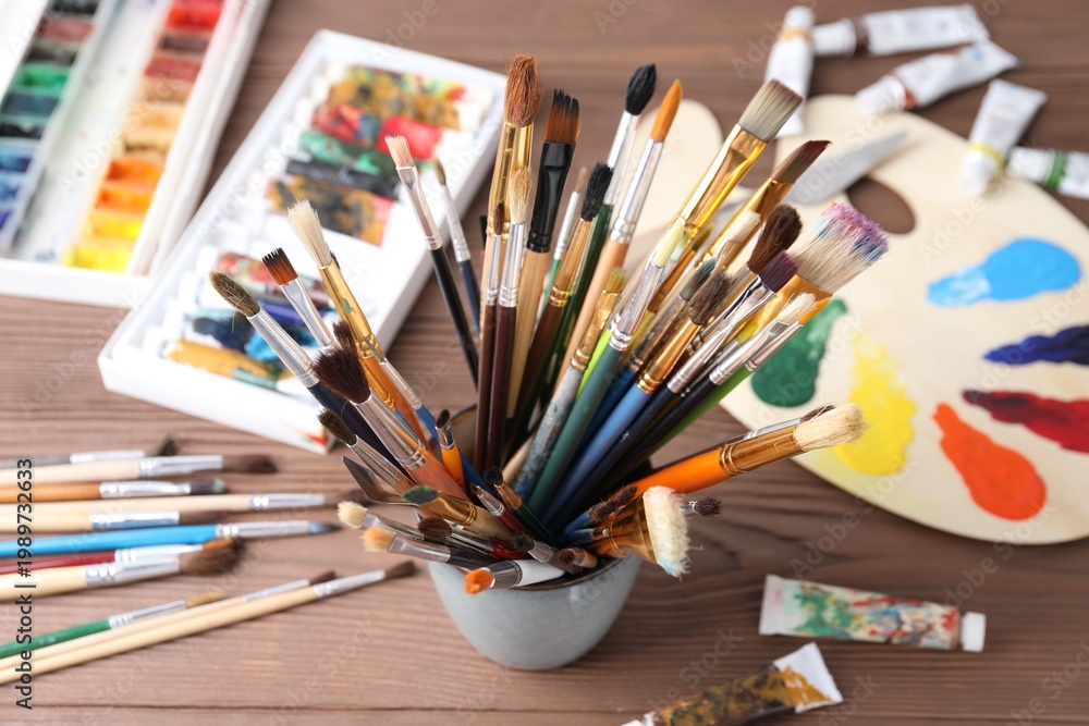 Obraz premium Paintbrushes in holder and paints on wooden table