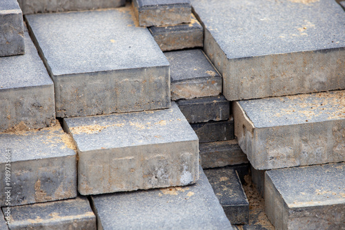 Quadro su tela Horizontal close-up perspective showing grey concrete paving stones laid in rows adjacent to a pile of construction sand base during pedestrian walkway installation
