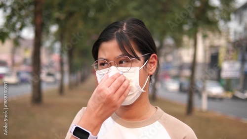 Side view of a young Asian girl wearing a protective face mask for PM 2.5 and air pollution prevention on a hazy city street background