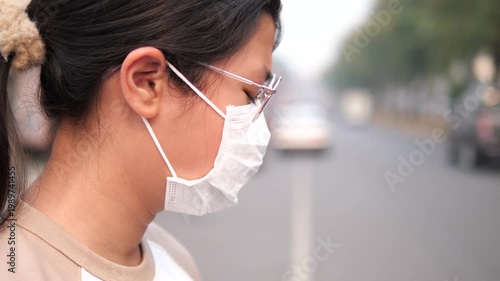 Side view of a young Asian girl wearing a protective face mask for PM 2.5 and air pollution prevention on a hazy city street background