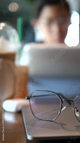 Vertical close-up of blue light blocking glasses on a digital tablet with a blurred young girl studying in the background, education and digital eye strain concept