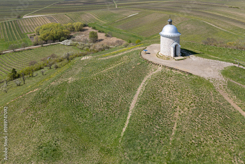An aerial view of the rotunda-style Chapel of St. Urban sitting atop the Hradištěk hill, surrounded by the geometric patterns of the South Moravian vineyards in springtime