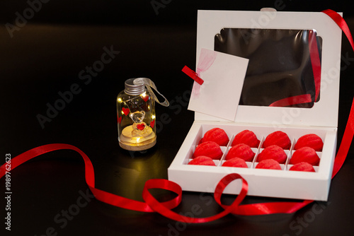 A white cardboard box with red shortcrust pastry nuts, with filling, on a black background, decorated with red ribbons and toys - a horse and a teddy bear in a jar