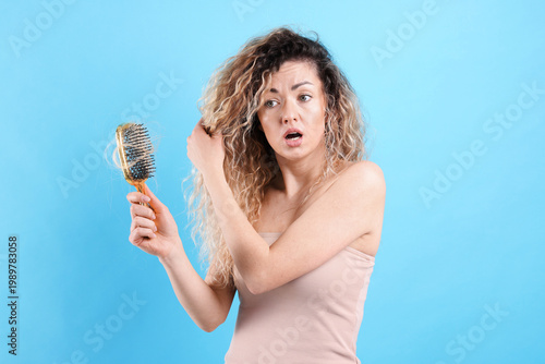 Foto Unhappy woman trying to brush her tangled hair on light blue background