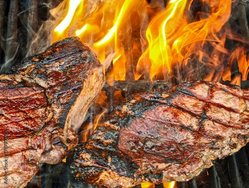 Two sirloin steaks grilling on barbecue with flames and smoke, close up of beef steaks cooking over open fire, juicy meat searing on grill, outdoor BBQ food preparation