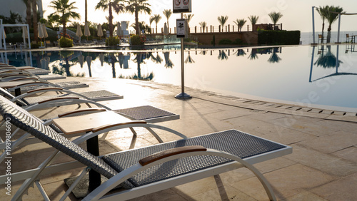 Schilderij op canvas Sunlit poolside with empty loungers and calm water