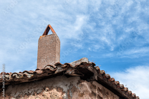 Old roof and chimney silhouetted against a blue sky with clouds