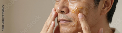 asian male gently applies rich night cream face warm soft indoor lighting shot