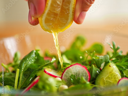 Close-up of Hands Squeezing Fresh Lemon over Gourmet Salad with Vibrant Colors