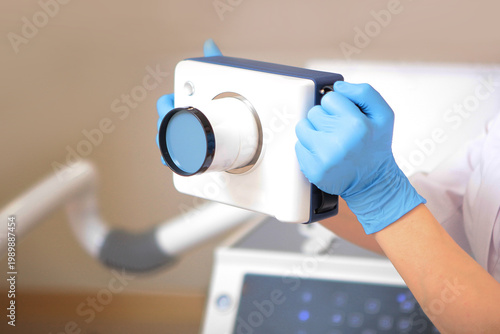 Dentist holds an X-ray machine in his hands to obtain images of teeth. X-ray machine in dentistry. Just hands. Hands in protective gloves.