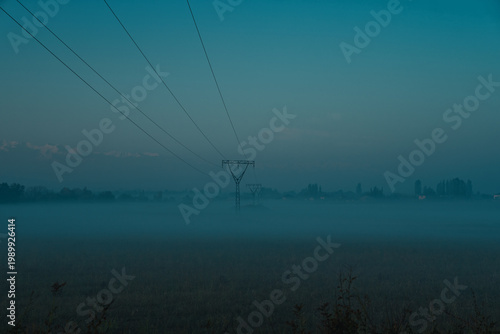 Foggy field with power lines and pylons in morning light