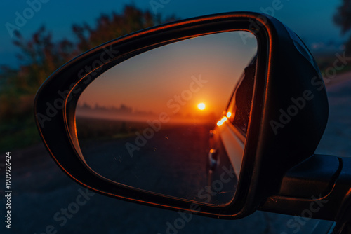 Car side mirror reflecting sunset road and landscape